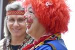 eine Dame im Clown-Kostüm mit roter Perücke und eine Indianerin im Hintergrund