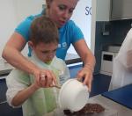 Eine Angestellte hilft einem Jungen beim Herstellen seiner Schokolade