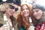 Drei breit grinsende Bürgerinnen mit Perücke und Bierflasche ausgestattet
