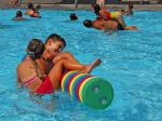 zwei Kinder amüsieren sich im Nichtschwimmerbereich mit einem Schwimmstab aus Schaumgummi. Im Hintergrund spielen weitere Kinder im Wasser