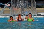 drei junge Mädchen, die unter einem Wasserpilz stehen und in die Kamera winken