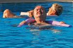 ein Herr geniesst die Sonne und entspannt mit einem Schwimmstab um den Schultern im Becken