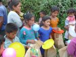 mehrere, einheimische Kinder, die mit Tellern in der Hand auf das Essen warten. Ein junges Mädchen spielt mit einem Luftballon