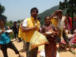Säcke mit Lebensmitteln werden an Einheimische verteilt. Im Vordergrund steht ein Helfer, der einer einheimischen Frau einen Sack reicht.