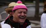 ein lachender Mann mit einer pink-gelben Bommelmütze