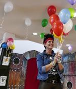 eine Mitarbeiterin des Rathauses hält mit einem breiten Lächeln einen Haufen Luftballons in der Hand. Im Hintergrund sieht man eine Burg-Kulisse