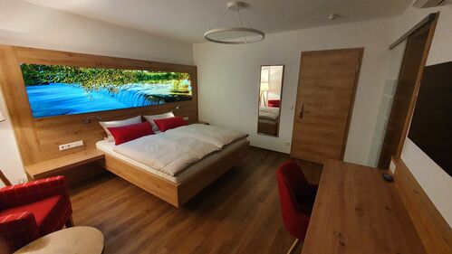 Der Adler - Hotelzimmer in hellem modernen Holz. Im Kopfteil des Bettes ist ein Leuchtbild. Wir blicken auf die Wutachkaskaten im Ortsteil Oberlauchringen.