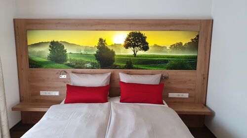 Der Adler - Hotelzimmer in hellem modernen Holz. Im Kopfteil des Bettes ist ein Leuc